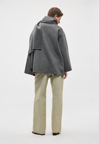 Hall halli villaseguga mantel kõrge kraega ja langeva seljaga. Sobitatud heledate beežide laiade pükstega. Sile tekstuur, minimalistlik disain.