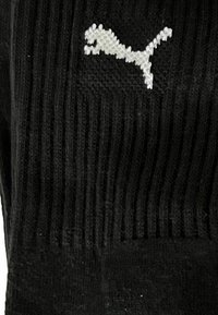 Schwarze gerippte Socke mit einem weißen gestickten Puma-Logo an der Seite. Das Material wirkt weich und strukturiert.