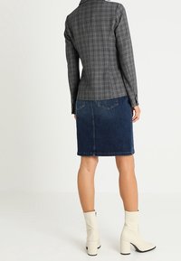 Šedá kostkovaná dolů přiléhavá blazer s dlouhými rukávy, v kombinaci s tmavě modrou tužkovou sukní. Bílé kotníkové boty s čtvercovými podpatky dotvářejí celý outfit.