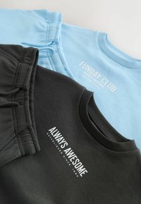 Deux sweats pliés, un noir avec le texte "ALWAYS AWESOME" et un pantalon noir assorti, et un autre bleu clair avec le texte "FUNDAY CLUB".
