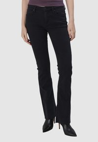 Jeans noires évasés en denim, dotés d'un design classique à 5 poches, de passants de ceinture et d'une taille mi-haute, associés à des talons noirs pointus.