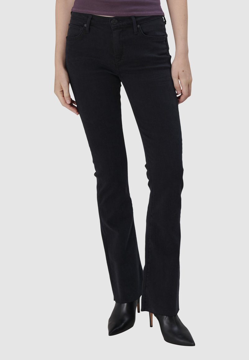 Jeans noires évasés en denim, dotés d'un design classique à 5 poches, de passants de ceinture et d'une taille mi-haute, associés à des talons noirs pointus.