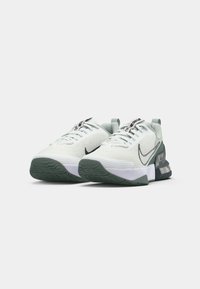 Nike športové topánky s bielym sieťovaným zvrškom, zelenými akcentmi a textúrovanou šedou podrážkou. Obsahujú výrazné čierne logo swoosh a šnurovanie.
