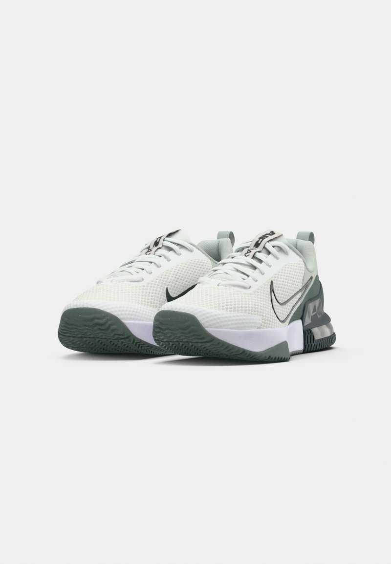 Zapatillas deportivas Nike con parte superior de malla blanca, acentos verdes y suela texturizada gris. Presentan un destacado logo de swoosh negro y cierre con cordones.