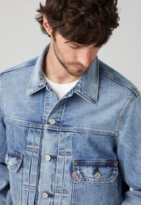 Denim jakna u svijetloplavoj boji s kopčanjem na gumbe, dva prednja džepa, kontrastnim šavovima i ovratnikom. Mekani, teksturirani materijal.