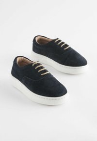Marinblå mockasneakers med vita gummisulor, rund tå och beige snören, med stickningsdetaljer och en slät inre foder.