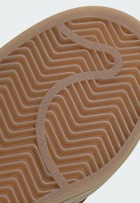 Gros plan d'une semelle de chaussure en caoutchouc marron avec un motif de bande de roulement ondulé et une rainure courbée sur la surface.