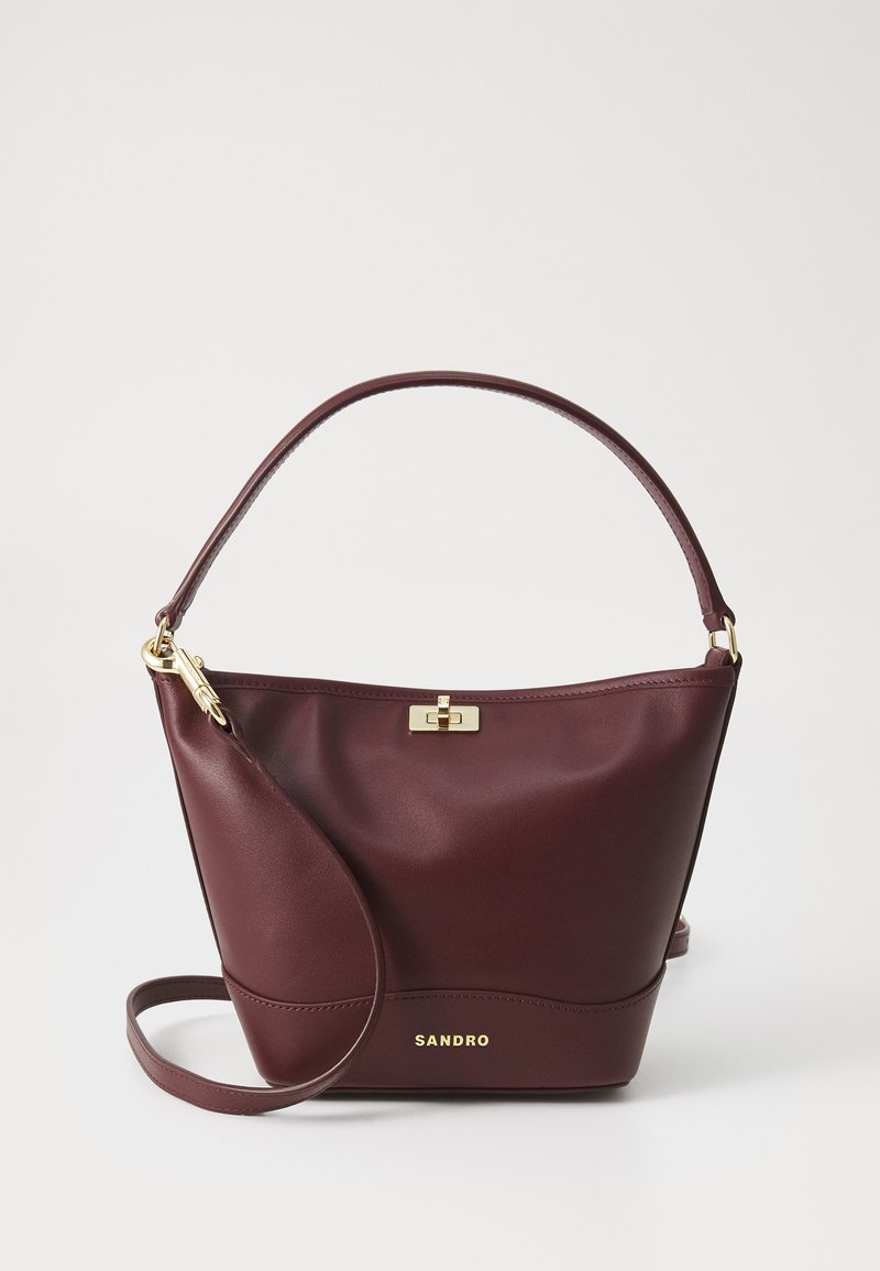 Borsa a mano in pelle borgogna con una forma strutturata, una base piatta, una maniglia arrotondata e dettagli in oro, inclusi una chiusura e il logo.