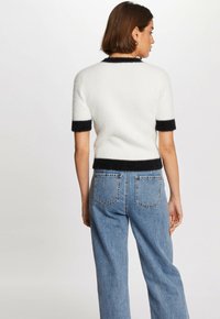 Suéter blanco de manga corta con ribete negro en las mangas y el dobladillo, fabricado con un material suave y esponjoso. Combinado con jeans de mezclilla claros de cintura alta.