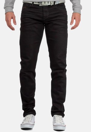 Schwarze Slim-Fit-Jeans aus Denim mit sichtbaren Stichen. Getragen mit einem grauen Sweatshirt und weißen Sneakers, mit einem enganliegenden Bund.