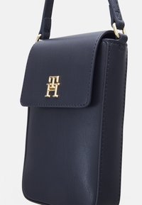 Bolso cruzado de cuero azul marino con cierre de solapa magnética, logo en tono dorado en la parte frontal y una textura suave.