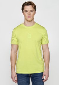 Tricou cu mânecă scurtă și guler rotund, de culoare verde lime strălucitor, realizat dintr-un material ușor; prezintă un logo subtil pe piept.