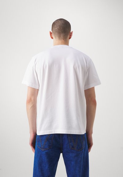 White cotton t-shirt with short sleeves, relaxed fit, and a straight neckline, paired with blue denim jeans featuring distinctive back pockets.