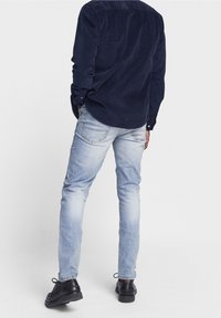 Marinblå kordfloss skjorta med lång ärm, kombinerad med ljusblå jeans och svarta snörskor. Strukturerad tyg med synliga sömmar och fickor.