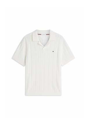 Polo a maniche corte in maglia bianca con texture a coste, colletto aperto e piccolo logo rosso, bianco e blu sul petto sinistro.