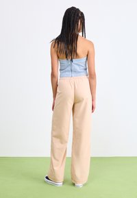 Light blue ribbed crop top with adjustable back zipper, paired with beige wide-leg pants. Model wears black sneakers. Plain background.