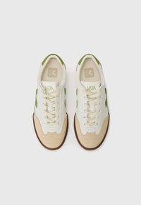 Λευκά αθλητικά παπούτσια με πράσινες λεπτομέρειες και μπεζ σουέντ στοιχεία. Κάτω μέρος από υφή δέρματος, στρογγυλή μύτη, κορδόνια μπροστά και καουτσούκ σόλα.