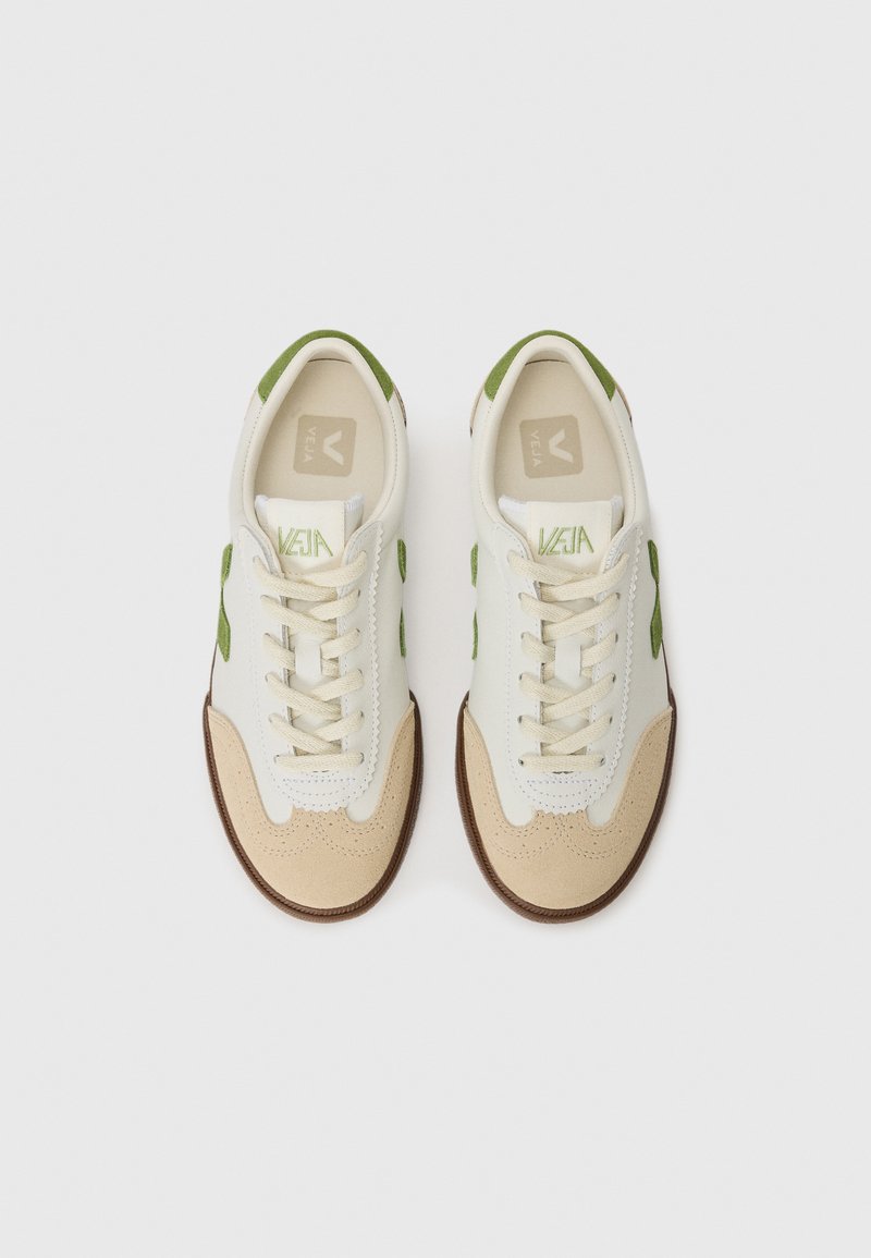 Baskets blanches avec des accents verts et des détails en daim beige. Tige en cuir texturé, bout arrondi, devant à lacets et semelle en caoutchouc.