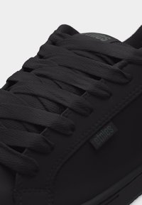 Κοντινό πλάνο μαύρου αθλητικού παπουτσιού με υφασμάτινες κορδόνια με υφή και ετικέτα υφάσματος "etnies" στην ομαλή πλευρική επιφάνεια.