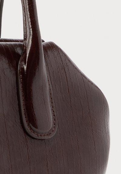 Donkere bruine leren handtas met gestikte handvatbevestiging, met een getextureerd oppervlak en een gebogen vorm tegen een neutrale achtergrond.