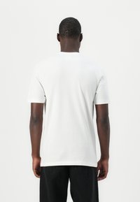 Hvid bomulds t-shirt med korte ærmer og rund hals. Stoffet ser glat ud med en afslappet pasform, båret med sorte jeans.