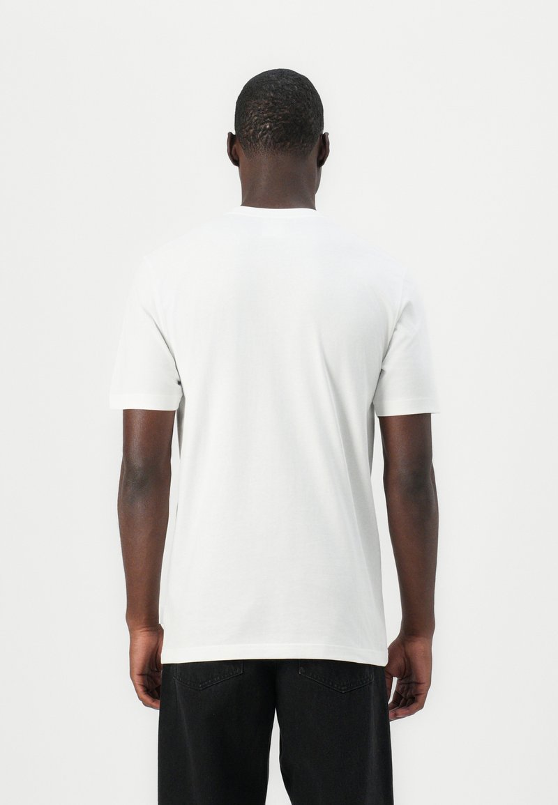 Camiseta de algodón blanca con mangas cortas y cuello redondo. La tela parece suave con un corte relajado, combinada con jeans negros.