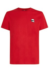 Rød bomulds T-shirt med korte ærmer og rund halsudskæring, der har et lille sort og hvidt grafisk ansigt med solbriller på venstre bryst.