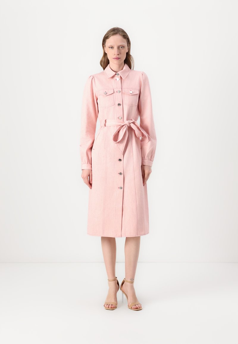 Rosa denimkjole med lange ermer, knappelukking foran, to brystlommer og knytbånd i midjen. Har en mellomhøyde og en strukturert design.