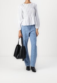 Blouse à manches longues rayée blanche et bleue avec taille smockée, associée à un jean à motifs bleu clair et un sac tote en cuir noir.