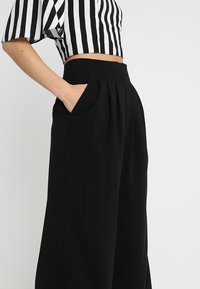 Černé kalhoty s širokými nohavicemi, záhyby a bočními kapsami. Kombinované s černobílým pruhovaným krátkým topem s krátkými rukávy.