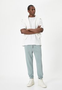 Vit kortärmad skjorta, mintgrön sweatpant och krämfärgade högklackade sneakers. Avslappnad outfit med en stickad vit tröja hängande över axlarna.