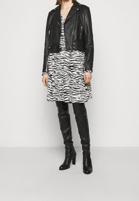 Giacca da moto in pelle nera su un vestito a righe zebrate bianche e nere con gonna svasata; abbinato a stivali neri sopra il ginocchio.