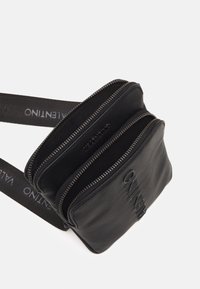 Černá crossbody taška se třemi zipovými přihrádkami; vyrobena z texturovaného materiálu; obsahuje popruh s logem a kovové zipové detaily.