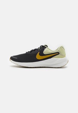 Baskets de sport noires et beiges avec un swoosh Nike doré, une semelle blanche rembourrée et des lacets noirs sur un fond blanc uni.