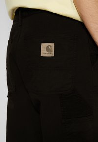 Svarta byxor med en stor bakficka med en tan märkning, texturerat tyg och kontrasterande paneldetalj.