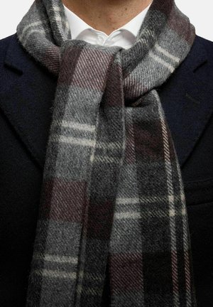 Ullscarf i grå, svart och vinröd rutmönster. Mjuk textur med fransade kanter, virad runt en krage ovanför en mörk kappa.