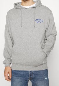 Šedá pulovrová mikina z měkkého materiálu s přední kapsou a nastavitelnou kapucí na šňůrku. Na hrudi modré logo "ATHLETIC Club".