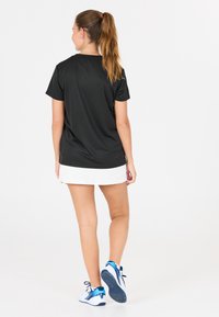 Sort kortærmet træningsbluse i glat stof, parret med en hvid nederdel. Modellen har blå og hvide sneakers med strukturerede såler på.