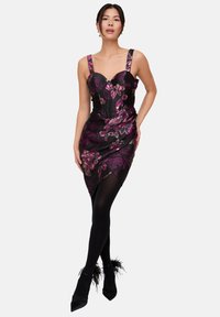 Schwarzes Kleid mit Blumenmuster und lila sowie goldenen Akzenten, figurbetontem Schnitt, herzförmigem Ausschnitt, breiten Trägern und asymmetrischem Saum. Kombinierbar mit schwarzen Strumpfhosen und High Heels.