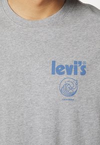 Gros plan d'un t-shirt gris avec un logo Levi's bleu et un motif circulaire de vague avec le mot California en dessous.
