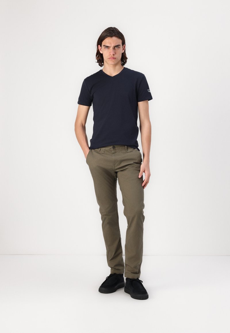 T-shirt a V con scollo profondo di colore blu navy abbinato a chino verde oliva e scarpe nere. L'outfit presenta una vestibilità rilassata con accenti di design minimi.