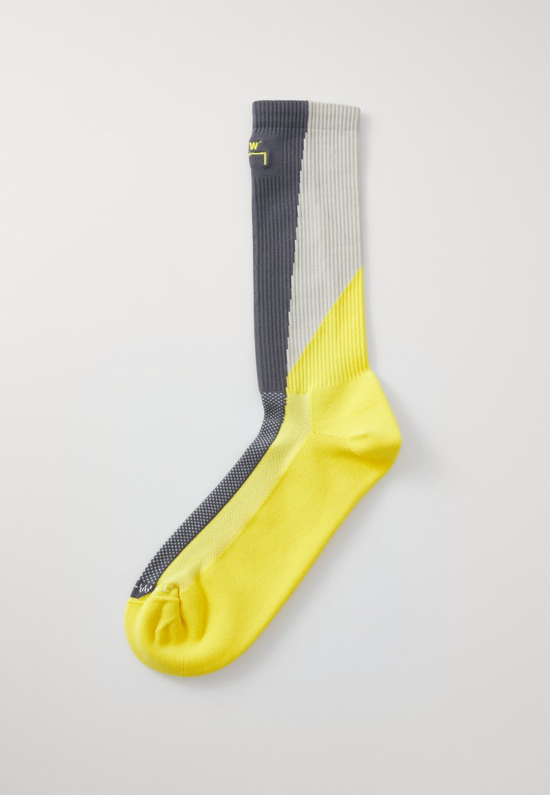 Knä-höga strumpor med ribbad design i grå, gul och ljusgrå sektioner. Tån och hälen är främst gula.