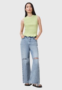 Ljusgrön smockad linne med scallopkant i kombination med ljusblå vida slitna jeans. Skorna är svarta sandaler med silverdetaljer.