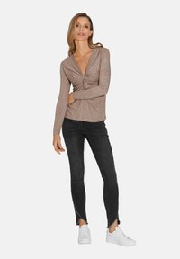 Hellbraunes Langarmoberteil mit einem verdrehten Vorderteil-Design, kombiniert mit schwarzen Skinny-Jeans mit ausgefransten Säumen und weißen Sneakers.