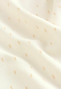 Világos krémszínű anyag finom mintázattal, apró, egyenletesen eloszló bézs pöttyökkel. Gyűrött megjelenés, ami fokozza a puha tapintást.