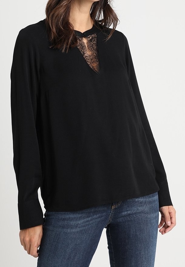 Blusa nera a maniche lunghe con pannello in pizzo all'collo, vestibilità rilassata e texture di tessuto liscia. Abbinata a jeans blu.