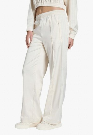 Donna che indossa pantaloni larghi color crema con vita elastica e tasca laterale con cerniera, abbinati a scarpe coordinate e top corto.
