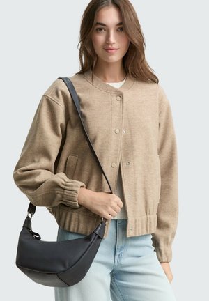Giacca bomber beige in lana con polsini elasticizzati e bottoni a pressione sul davanti, abbinata a una borsa a spalla nera texture. Indossa jeans azzurri.