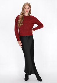 Pull en tricot rouge avec un motif texturé, associé à une jupe en satin noir élégante. Le mannequin porte des bottes noires à talons.