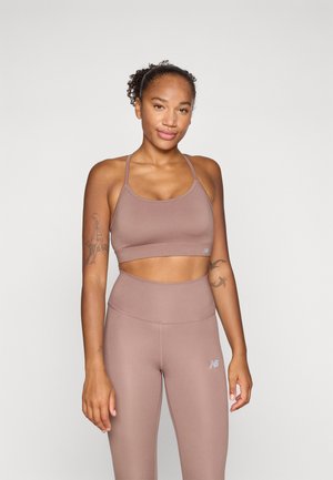 Brązowy sportowy top crop i legginsy z wysokim stanem, wykonane z gładkiego materiału. Zauważalny detal z logo na legginsach. Prosty, funkcjonalny design.